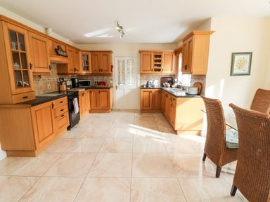 A kitchen with wooden cabinets tiled floor and a glass dining table with wicker chairs at Seascape Lodge in Kenmare County Kerry