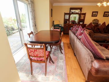 A dining table with chairs on a rug next to a sofa with cushions and a wooden cabinet in a living room at Seascape Lodge in Kenmare County Kerry