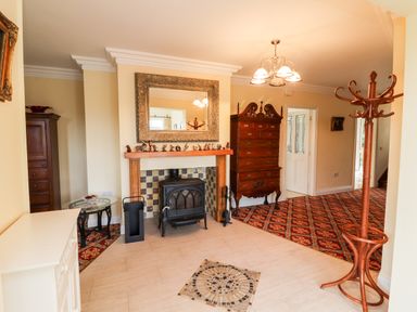 An entryway with a fireplace and stove a wooden chest of drawers tall coat rack and a small glass table at Seascape Lodge in Kenmare County Kerry