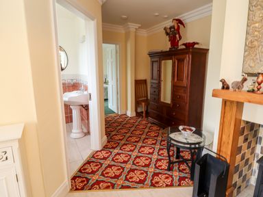 A hallway with a patterned carpet a wooden armoire a wooden chair a glass table and a fireplace at Seascape Lodge in Kenmare County Kerry