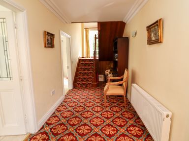 A hallway with patterned carpet a wooden chair a bookshelf and stairs leading up at Seascape Lodge in Kenmare County Kerry