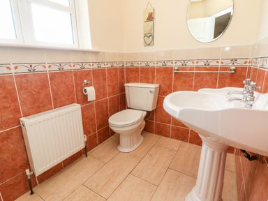 A bathroom with a toilet sink radiator and a circular mirror at Seascape Lodge in Kenmare County Kerry