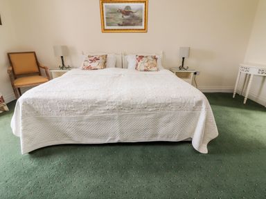 A bedroom with a double bed covered with a white quilt and floral pillows two bedside tables with lamps a wooden chair and a white corner table at Seascape Lodge in Kenmare County Kerry