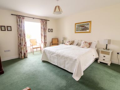 A bedroom with a large bed two chairs and floral curtains at Seascape Lodge in Kenmare County Kerry