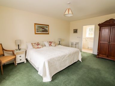 A bedroom with a double bed two bedside tables a wooden wardrobe a chair and a door leading to a bathroom at Seascape Lodge in Kenmare County Kerry
