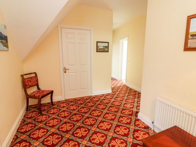 A hallway with patterned carpet a wooden chair paintings on the wall a white door and radiator at Seascape Lodge in Kenmare County Kerry