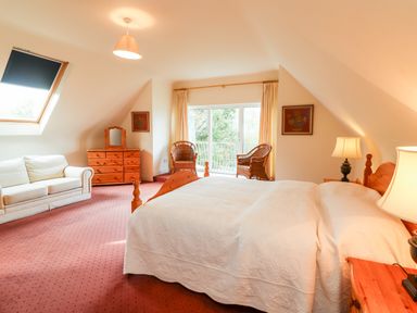 A bedroom with a bed sofa dresser wicker chairs and lamps at Seascape Lodge in Kenmare County Kerry