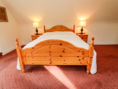 A bedroom with a wooden bed and two bedside tables with lamps at Seascape Lodge in Kenmare County Kerry