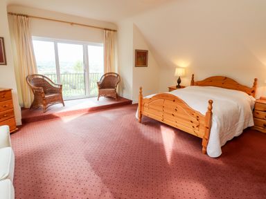 A bedroom with a wooden bed a white bedspread two wicker chairs near sliding glass doors and a red carpet at Seascape Lodge in Kenmare County Kerry