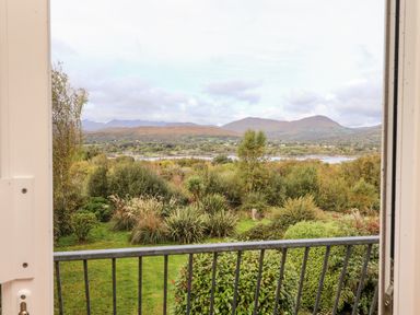 A view of a garden with bushes and trees looking out to hills and a body of water from a balcony at Seascape Lodge in Kenmare County Kerry