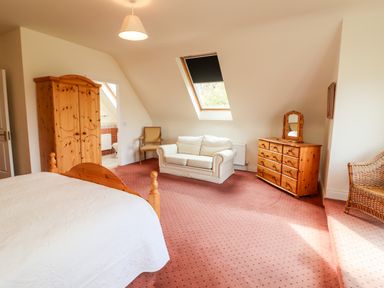 A bedroom with a wooden wardrobe a white sofa a dresser with a mirror a chair and a bed at Seascape Lodge in Kenmare County Kerry