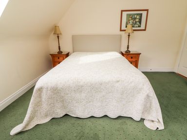 A bedroom with a bed covered in a white quilt flanked by two wooden nightstands with lamps and a framed painting on the wall at Seascape Lodge in Kenmare County Kerry