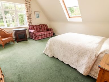 A bedroom with a bed covered in a white quilt a red patterned sofa a wicker chair a wooden nightstand and a large window at Seascape Lodge in Kenmare County Kerry
