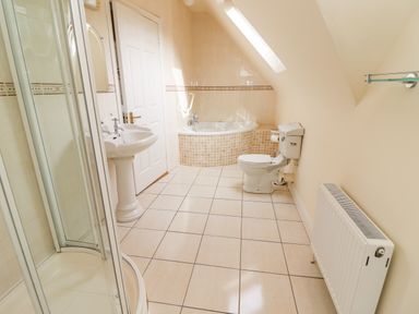 A bathroom with a shower, sink, bathtub, toilet, radiator, and tiled floor at Seascape Lodge in Kenmare County Kerry