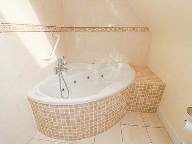 A corner bathtub with beige tiled surround and a grab bar on wall at Seascape Lodge in Kenmare County Kerry