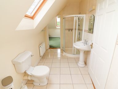 A bathroom with a toilet, pedestal sink, and corner shower under a sloped ceiling at Seascape Lodge in Kenmare County Kerry