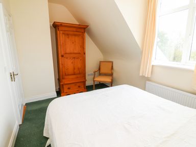 A bedroom with a bed a wooden wardrobe a chair and a window at Seascape Lodge in Kenmare County Kerry