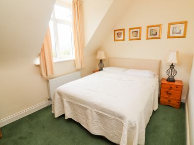 A bedroom with a double bed two bedside tables with lamps four framed pictures on the wall and a window with curtains at Seascape Lodge in Kenmare County Kerry