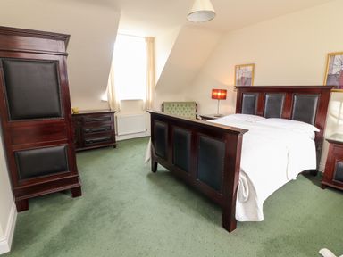 A bedroom with a bed a green armchair a dresser a wardrobe and two framed pictures on the wall at Seascape Lodge in Kenmare County Kerry