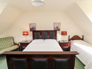 A bedroom with a double bed and a single bed with bedside tables and lamps and a green sofa at Seascape Lodge in Kenmare County Kerry