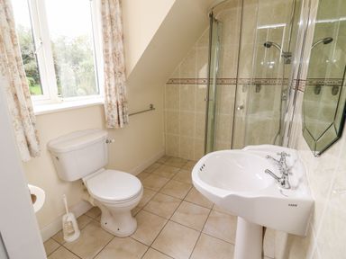 A bathroom with a toilet near a window and a sink opposite a glass shower enclosure at Seascape Lodge in Kenmare County Kerry