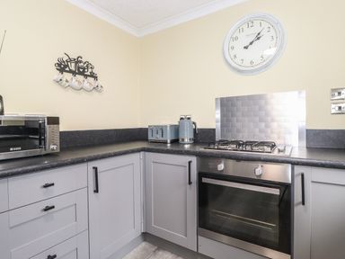 A kitchen corner with grey cabinets a microwave toaster kettle wall clock and a gas stove at Alfresco Lodge in Skiptory Howe 37B White Cross Bay near Windermere