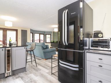 A kitchen and living area with a black refrigerator a microwave a bar stool and blue sofas at Alfresco Lodge in Skiptory Howe 37B White Cross Bay near Windermere