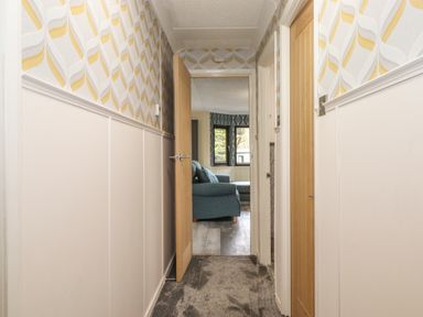 A hallway with patterned wallpaper and two wooden doors leading to a living room at Alfresco Lodge Skiptory Howe 37B White Cross Bay near Windermere