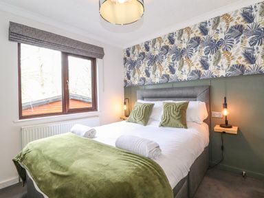A bedroom with a double bed green pillows green blanket and leaf patterned wallpaper at Alfresco Lodge in Skiptory Howe 37B White Cross Bay near Windermere