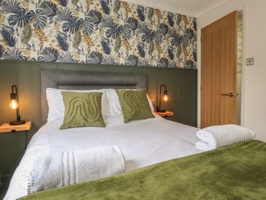 A bedroom with a double bed green pillows bedside lamps and a wooden door at Alfresco Lodge Skiptory Howe 37B White Cross Bay near Windermere