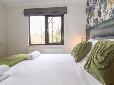 A bedroom with a bed with green pillows and a window with a grey blind at Alfresco Lodge Skiptory Howe 37B White Cross Bay near Windermere