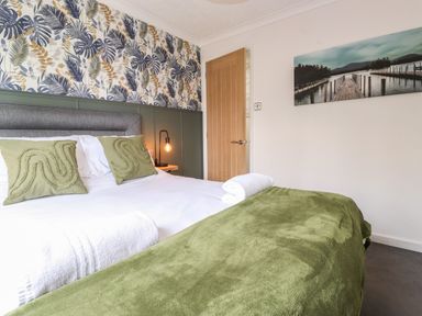A bedroom with a bed with green pillows and blanket a wooden door and a landscape painting on the wall at Alfresco Lodge Skiptory Howe 37B White Cross Bay near Windermere