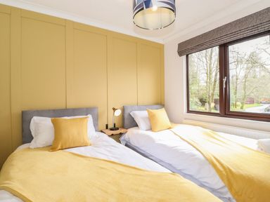 A bedroom with two single beds with yellow throws and pillows a bedside table and a window with blinds at Alfresco Lodge Skiptory Howe 37B White Cross Bay near Windermere
