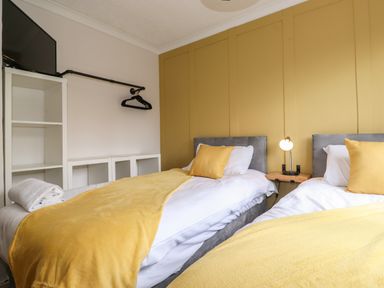 A bedroom with two single beds with yellow blankets and pillows a small lamp a white shelving unit and a wall-mounted TV at Alfresco Lodge Skiptory Howe 37B White Cross Bay near Windermere