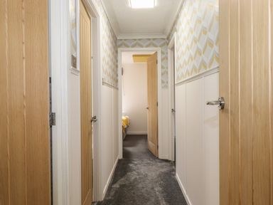 A hallway with carpet flooring wooden doors and patterned wallpaper at Alfresco Lodge in Skiptory Howe 37B White Cross Bay near Windermere