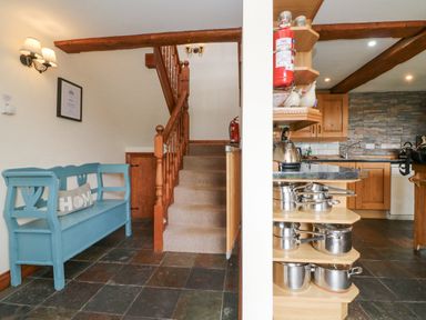 An entryway with a blue wooden bench and a staircase next to a kitchen with wooden cabinets and stainless steel pots at Apple Barn in South Molton