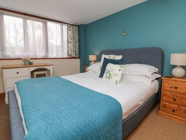 A bedroom with a double bed, bedside tables with lamps, a desk under a window with curtains at Apple Barn in South Molton