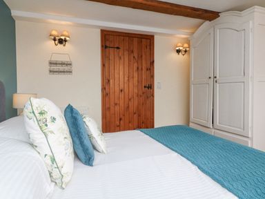 A bedroom with a bed with cushions and a blue throw a wooden door wall lamps and a white wardrobe at Apple Barn in South Molton