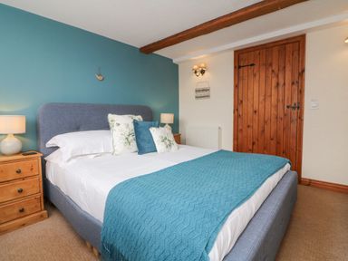 A bedroom with a bed with pillows and a blue throw blanket next to wooden bedside tables and a wooden door at Apple Barn in South Molton