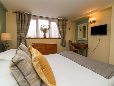 A bedroom with a bed pillows and throw blanket a wooden dresser a desk chair and a wall-mounted TV at Apple Barn in South Molton