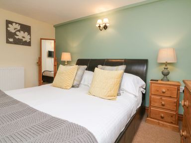 A bedroom with a double bed cushions bedside tables lamps a mirror and a painting at Apple Barn in South Molton