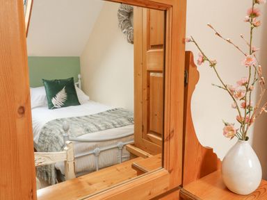 A bedroom with a bed reflected in a wooden mirror and a vase with flowers on a wooden surface at Apple Barn in South Molton