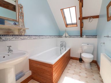 A bathroom with a bathtub with wooden paneling a toilet a sink a skylight window and wooden beams at Apple Barn in South Molton