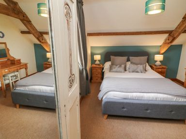 A bedroom with a double bed flanked by two wooden nightstands with lamps a dressing table and mirror at Apple Barn in South Molton
