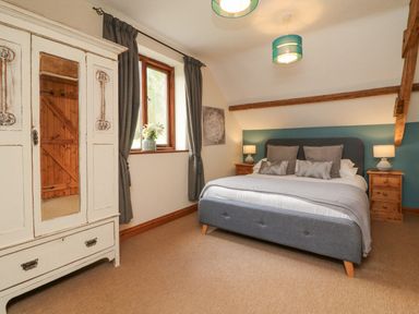 A bedroom with a double bed bedside tables lamps a window with curtains and a white wardrobe at Apple Barn in South Molton
