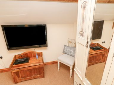 A wooden cabinet with a television remote on top a chair with a cushion and a wardrobe with a mirrored door in a small room at Apple Barn in South Molton