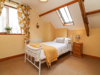A bedroom with a single white metal bed with pillows and a yellow throw a wooden bedside table with a lamp a window with yellow patterned curtains and a skylight at Apple Barn in South Molton