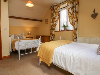 A bedroom with two single beds and a window with patterned curtains at Apple Barn South Molton
