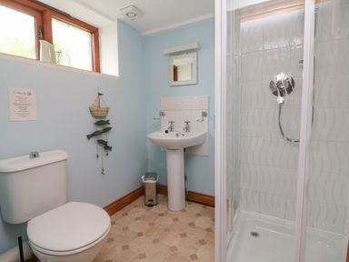 A bathroom with a toilet, pedestal sink, mirror, shower enclosure, and a window with decorative items at Apple Barn in South Molton