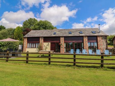 A stone and wood house with multiple windows blue chairs and a wooden fence on a lawn at Apple Barn in South Molton